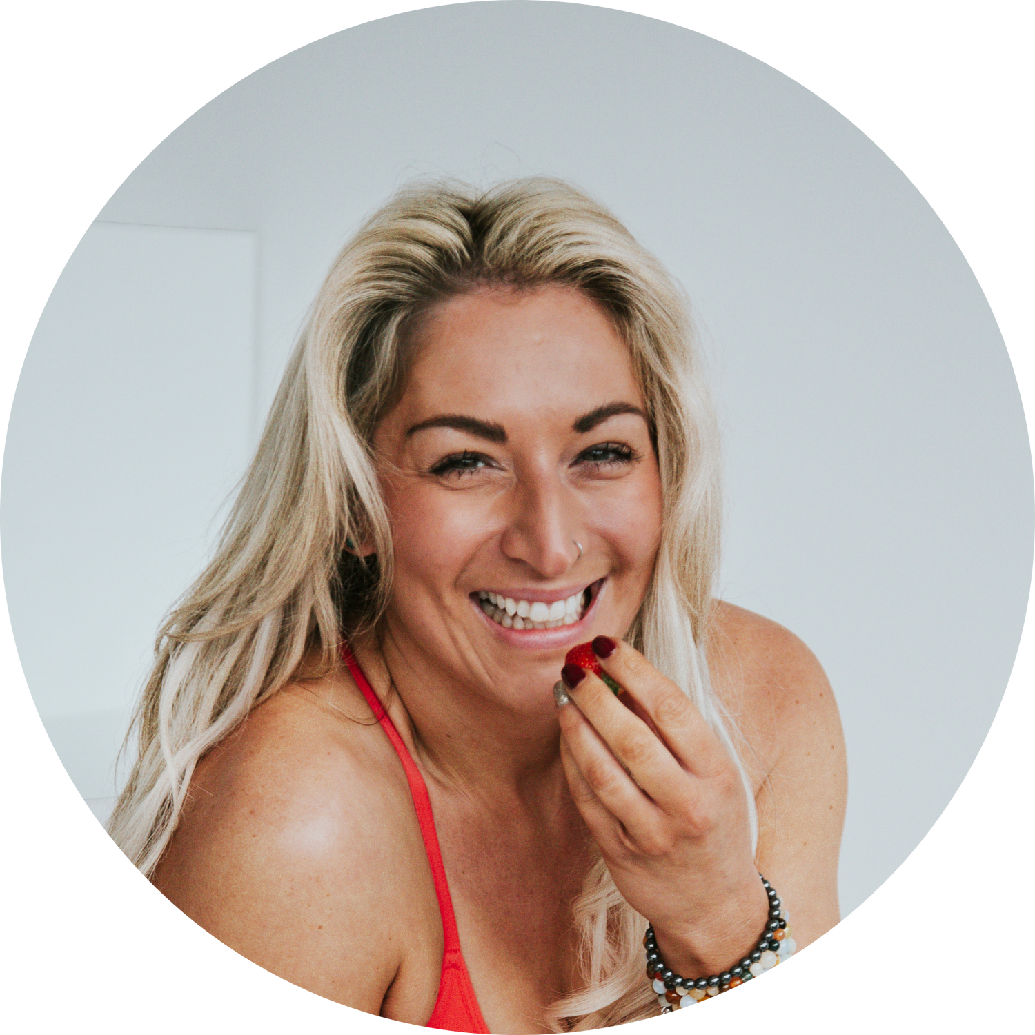 Smiling blonde woman in red top holding a strawberry near her mouth in a circular portrait