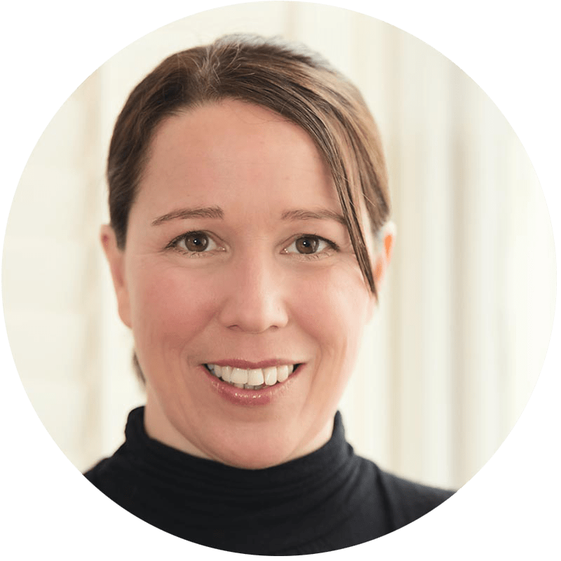 Smiling headshot of a woman with brown hair wearing a black turtleneck, circular crop, soft indoor background.